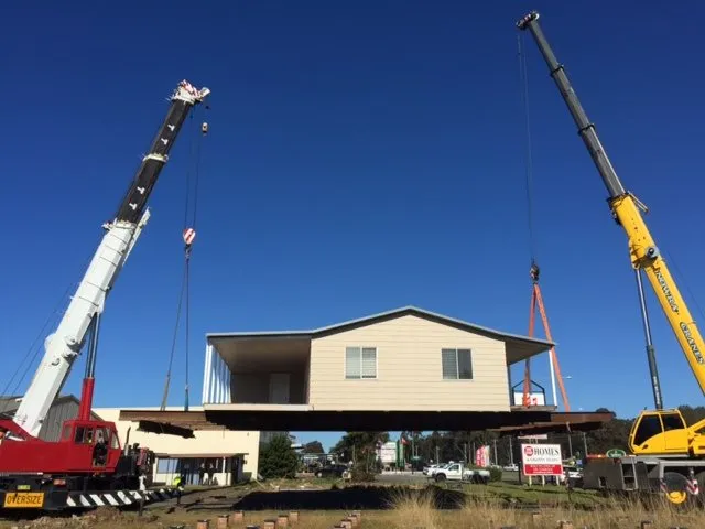 Two cranes lifting a two-storey house