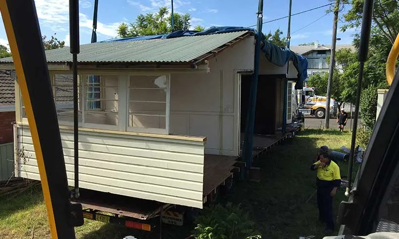 House loaded onto a truck beside the crane