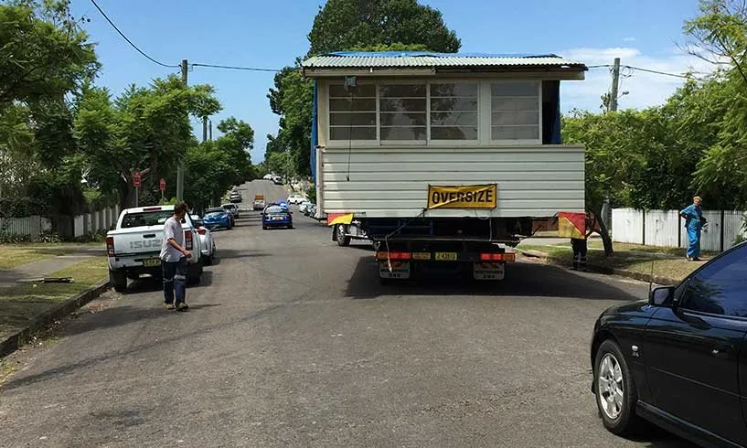 Weatherboard house on a truck, moving down a suburban street