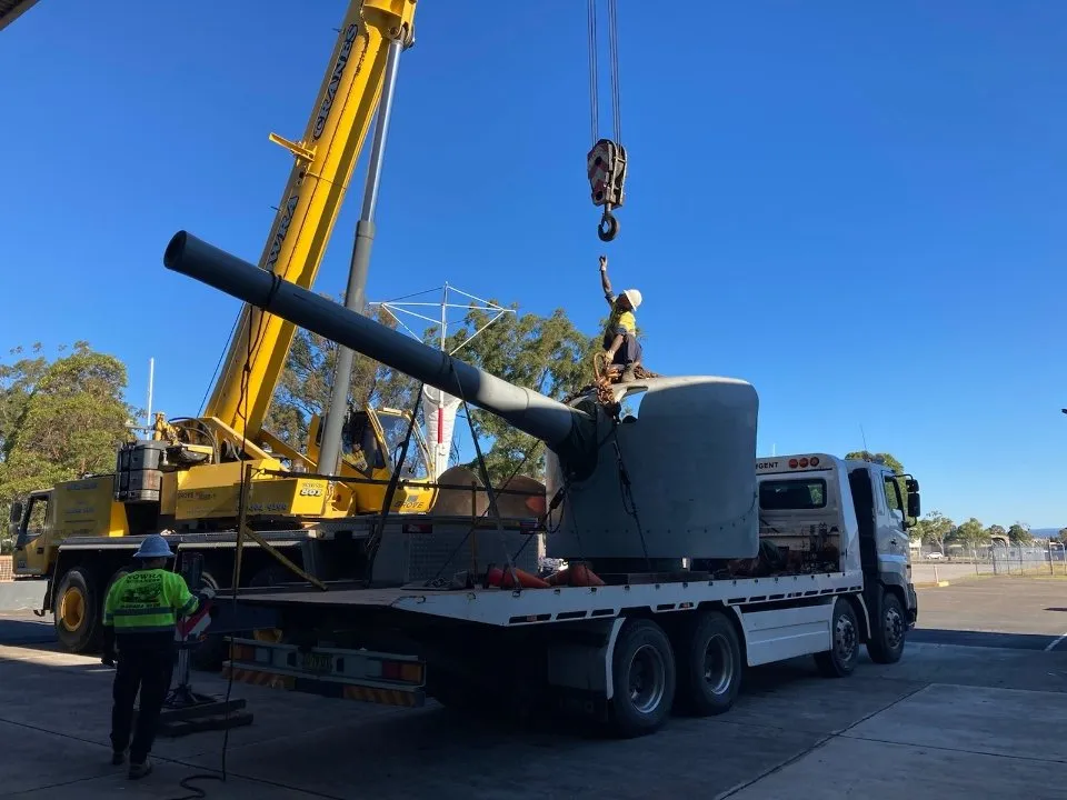 Crane lifting a naval gun turret onto a truck