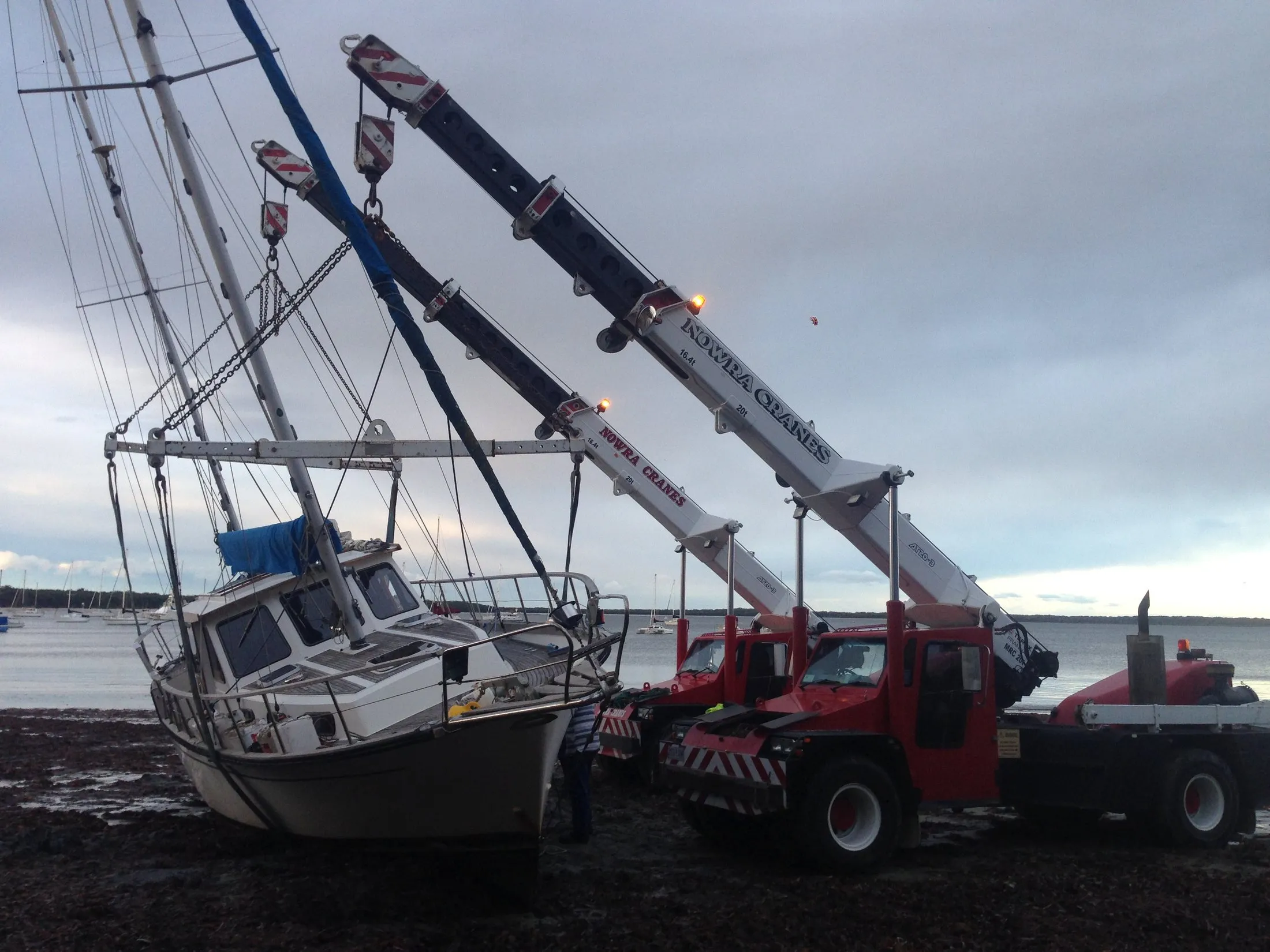 Two cranes recovering a yacht from the shoreline with slings
